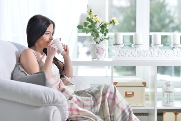 Jonge vrouw die in een fauteuil zit en thee drinkt in de lichte kamer