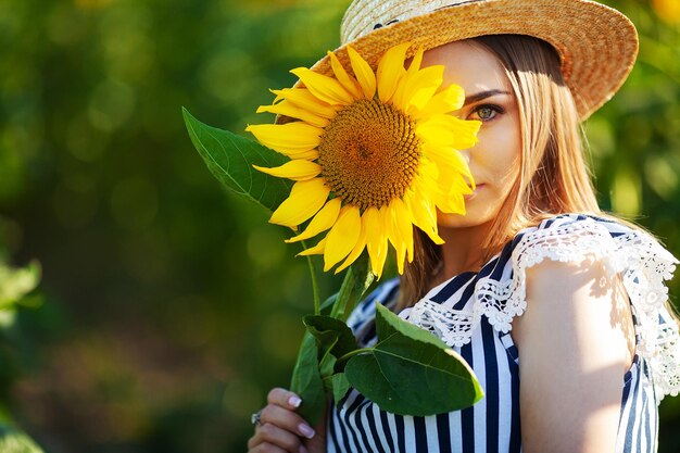 Jonge vrouw die in het veld naar de zon loopt en een zonnebloem vasthoudt