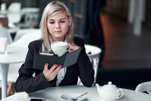 Jonge vrouw die in koffie een ebook lezen en koffie drinken