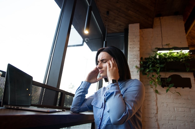 Jonge vrouw die in koffiehuisvoorzijde van laptop werkt die aan chronische dagelijkse hoofdpijn lijdt