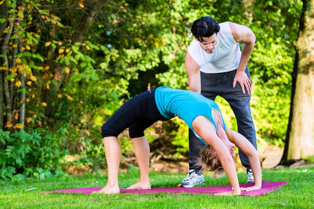 Jonge vrouw die in openlucht yoga met trainer doet