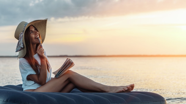 Jonge vrouw die in strohoed poëzie op het strand samenstelt. Inspiratie concept