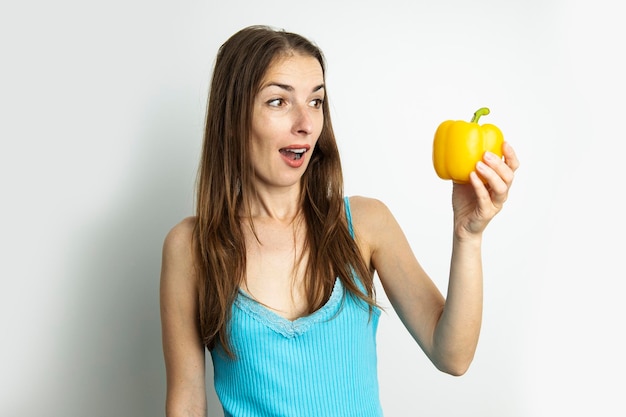 Jonge vrouw die in verrassing gele paprika bekijkt die op witte achtergrond wordt geïsoleerd