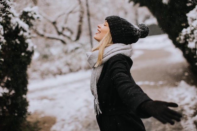 Jonge vrouw die in warme kleren in sneeuw geniet