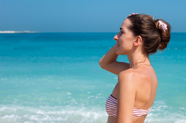 Jonge vrouw die in zwempak haar hoofd houdt dat naar de zee kijkt