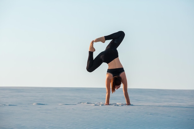 Jonge vrouw die inversie balancerend yoga beoefent, handstand op zand