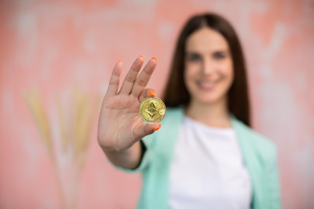 Jonge vrouw die lacht met cryptocurrency als elektronische betaling op roze achtergrond