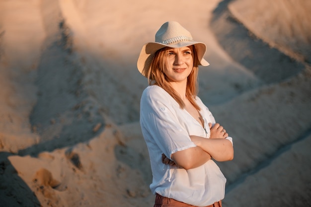 Jonge vrouw die lacht op het strand. Een meisje een zanderig met een hoed. Mooi meisje in een zandgroeve.