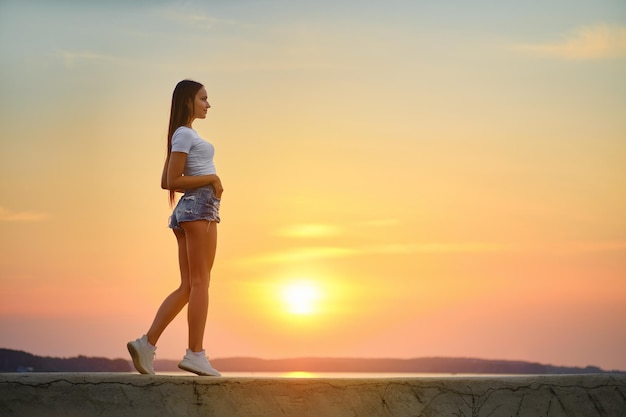 Jonge vrouw die langs een pier loopt tijdens de zonsondergang