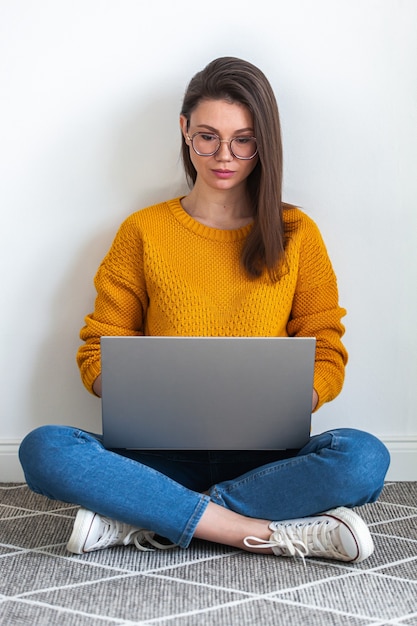 Jonge vrouw die laptop gebruikt die op tapijt zit