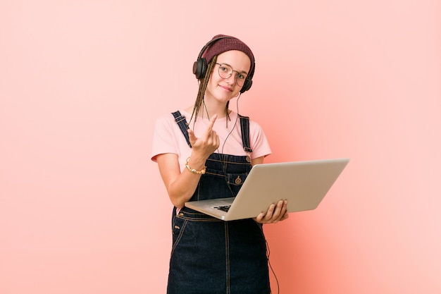 Jonge vrouw die laptop houdt die met vinger op u richt alsof uitnodigend dichterbij kom.