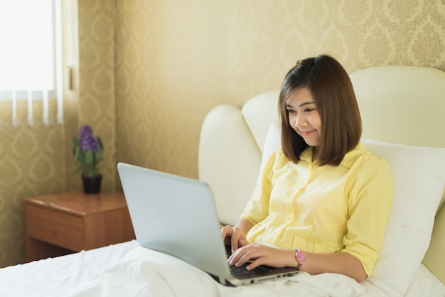 Jonge vrouw die laptop in slaapkamer thuis met behulp van