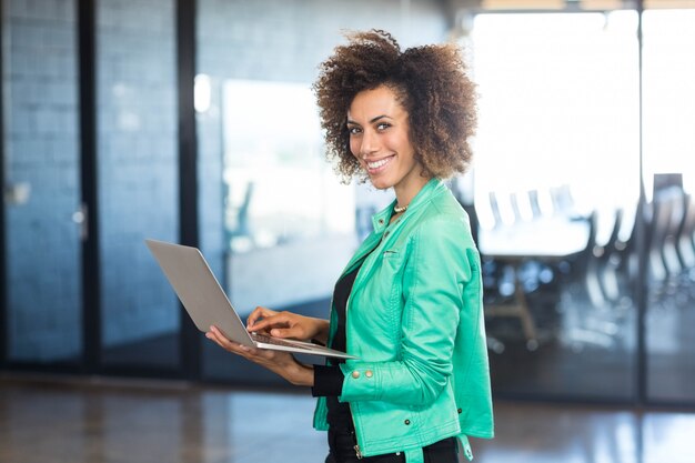 Jonge vrouw die laptop voor conferentieruimte in het bureau met behulp van