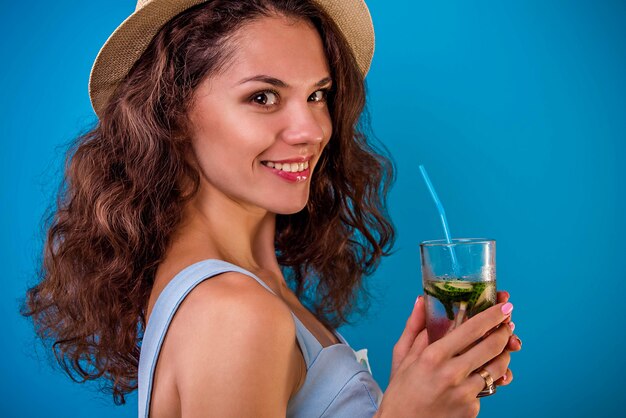 Jonge vrouw die limonade op blauwe muur drinkt