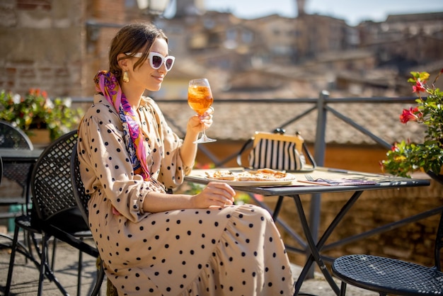Jonge vrouw die luncht met pizza en wijn in het openluchtrestaurant in de stad Siena