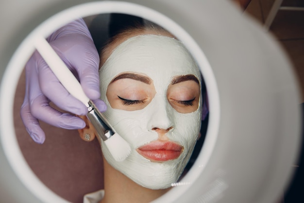 Jonge vrouw die masker van klei op gezicht in beauty spa toepast