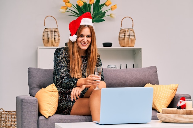 Jonge vrouw die met de hoed van de Kerstman een videogesprek voert met haar familie om Kerstmis te vieren.