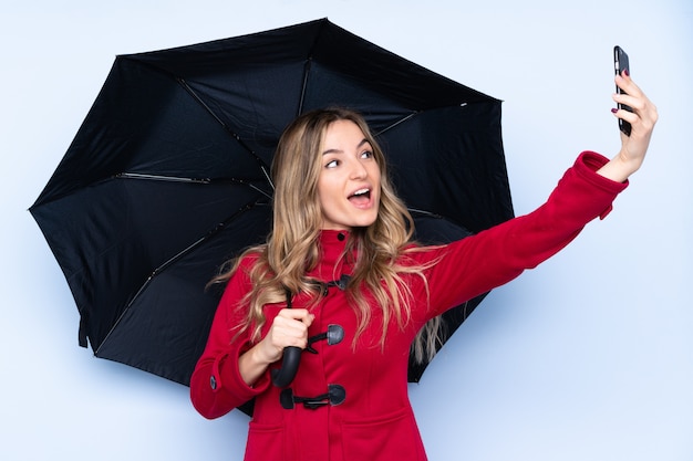 Jonge vrouw die met de winterjas een paraplu en mobiel houdt