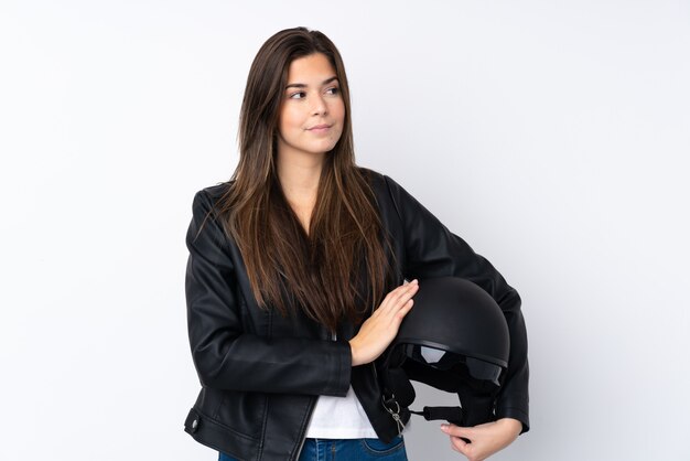 Jonge vrouw die met een motorhelm over geïsoleerde witte muur een idee denkt