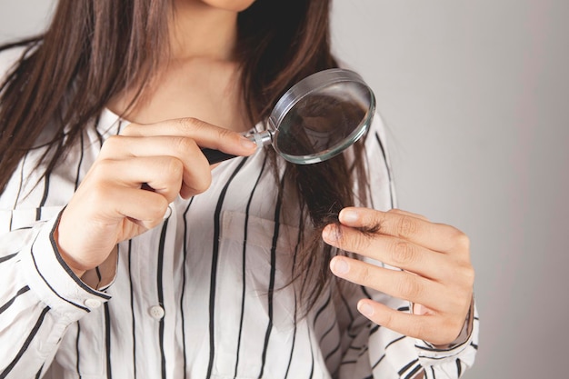 Jonge vrouw die met een vergrootglas naar haar haar kijkt