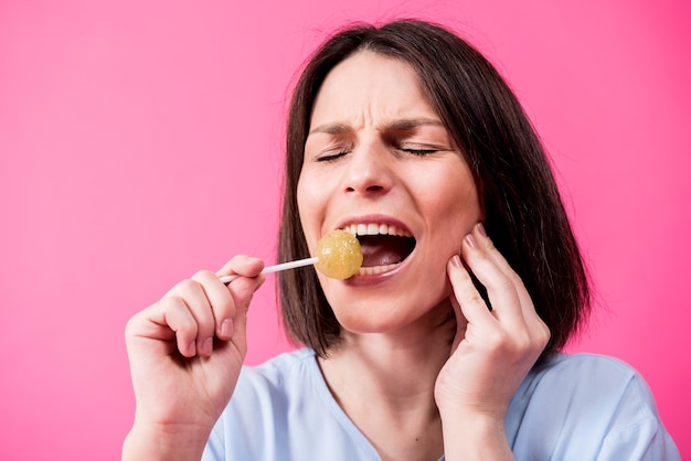 Foto jonge vrouw die met gevoelige tanden zoete lolly op kleurenachtergrond eet