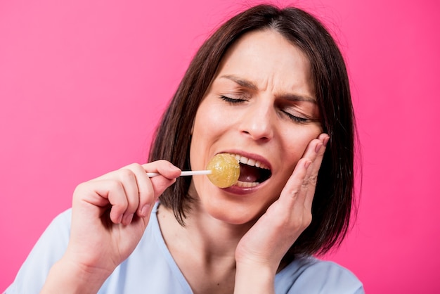 Jonge vrouw die met gevoelige tanden zoete lolly op kleurenachtergrond eet