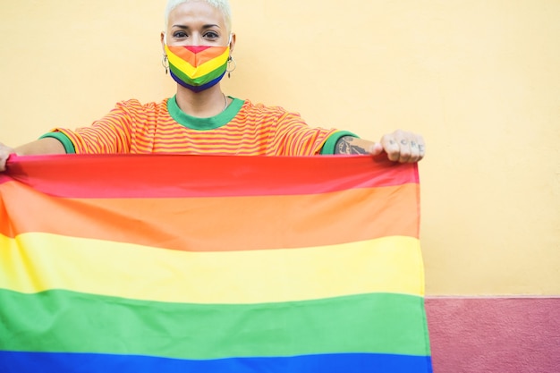 Jonge vrouw die met gezichtsmasker een gay pride-regenboogvlag houdt