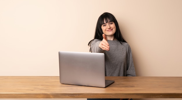 Jonge vrouw die met haar laptop het schudden handen voor het sluiten van een goede overeenkomst werkt