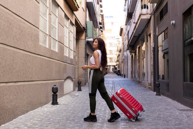 Foto jonge vrouw die met koffer op straat loopt