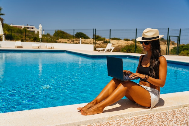 Jonge vrouw die met laptop dichtbij het zwembad werkt