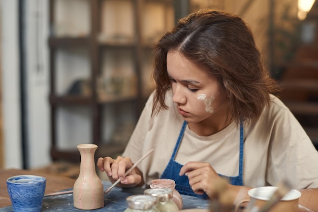 Jonge vrouw die met penseel zelfgemaakte kruik of pot schildert