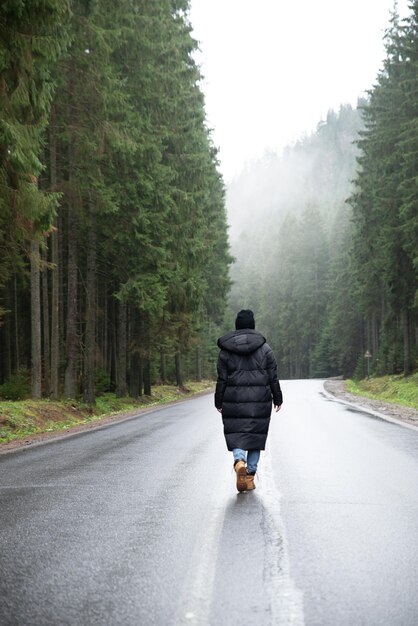 Jonge vrouw die midden op de weg staat in het bos van de winterbergen