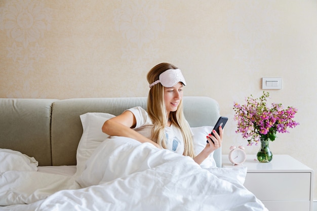 Jonge vrouw die mobiele telefoon op het bed met behulp van