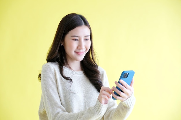 Jonge vrouw die mobiele telefoon vasthoudt en glimlacht terwijl ze over een geïsoleerde gele achtergrond staat