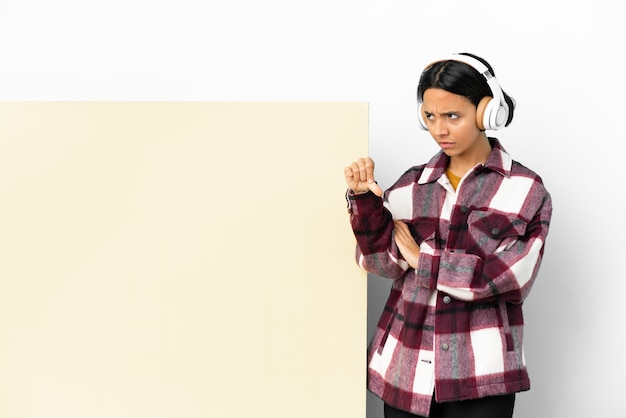 Jonge vrouw die muziek luistert met een groot leeg bordje over geïsoleerde achtergrond met duim omlaag met negatieve uitdrukking