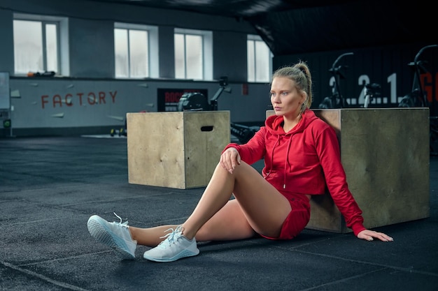 Jonge vrouw die na haar training in de buurt van een doos in de sportschool zit en wegkijkt