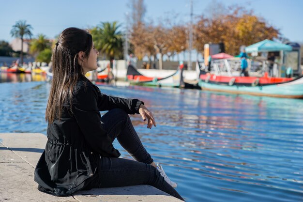 Jonge vrouw die naar de lucht kijkt terwijl ze op de grond zit naast een waterkanaal in Aveiro Portugal