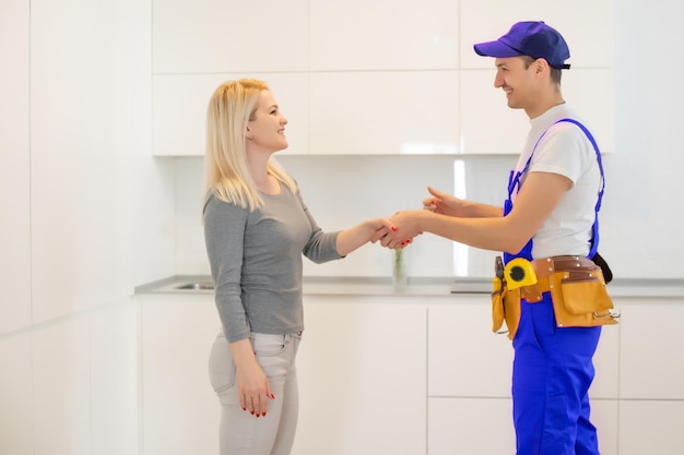 Jonge vrouw die naar mannelijke technicus kijkt die de vaatwasser in de keuken controleert.