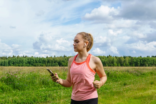 Jonge vrouw die naar muziek luistert of berichten leest tijdens het joggen langs een pad door een weiland