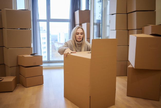 Jonge vrouw die nieuwe plaats verplaatst en concept herstelt Gelukkige jonge vrouw met veel kartonnen dozen die zitten