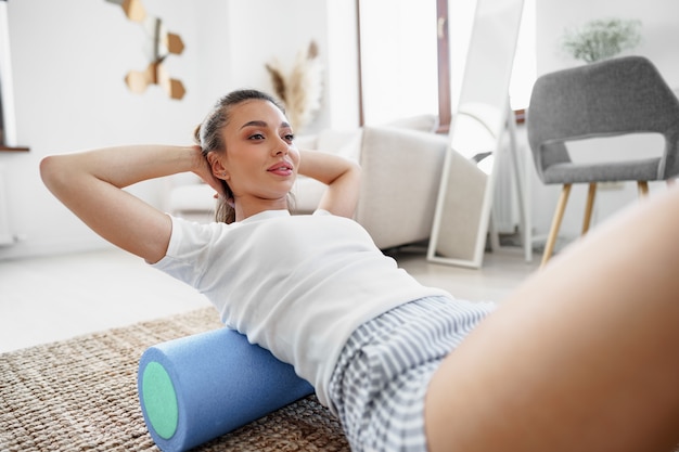 Jonge vrouw die oefening met gymnastiekbroodje op de vloer thuis doet