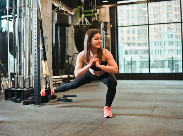 Jonge vrouw die oefening voor benen op trx doet bij gymnastiek.