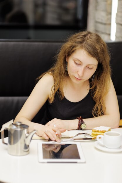 Jonge vrouw die of op haar tabletcomputer in een koffie werkt studing