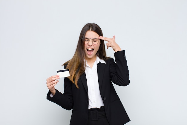 Jonge vrouw die ongelukkig en beklemtoond kijken, zelfmoordgebaar die kanonteken met hand maken, die aan hoofd met een creditcard richten