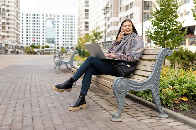 Jonge vrouw die online aan laptop werkt in het park op een bank freelance werkconcept