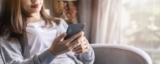 Jonge vrouw die op bank bij woonkamer liggen en celtelefoon thuis met behulp van