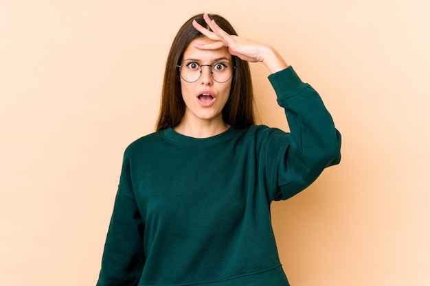 Jonge vrouw die op beige ver weg het houden van hand op voorhoofd kijkt.