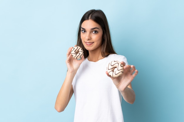 Jonge vrouw die op blauwe muur wordt geïsoleerd die donuts met gelukkige uitdrukking houdt