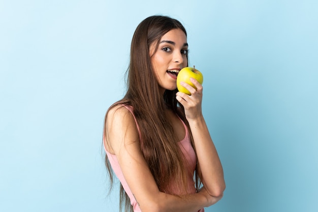 Jonge vrouw die op blauwe muur wordt geïsoleerd die een appel eet