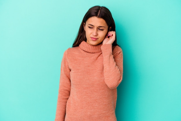 Jonge vrouw die op blauwe muur wordt geïsoleerd die oren bedekt met vingers, gestrest en wanhopig door een luid ambient